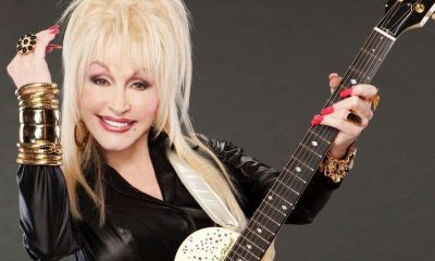 A photo of Dolly Parton in a black color outfit, holding a guitar.